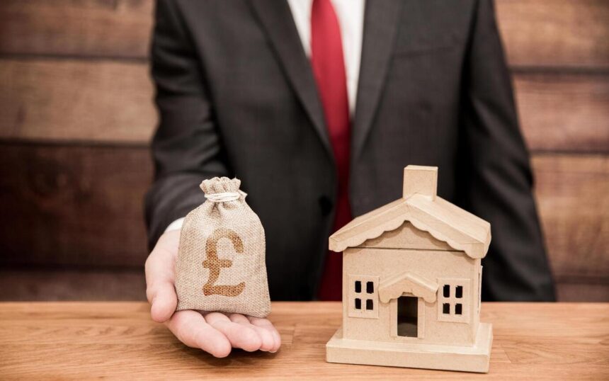 Concept showing cost house value increase with solar panel installation. Man holding small bag with pound sign next to small model of house. Blog image for More Than Solar Panels